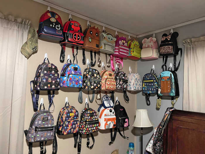 21 mini backpacks hanging on a wall